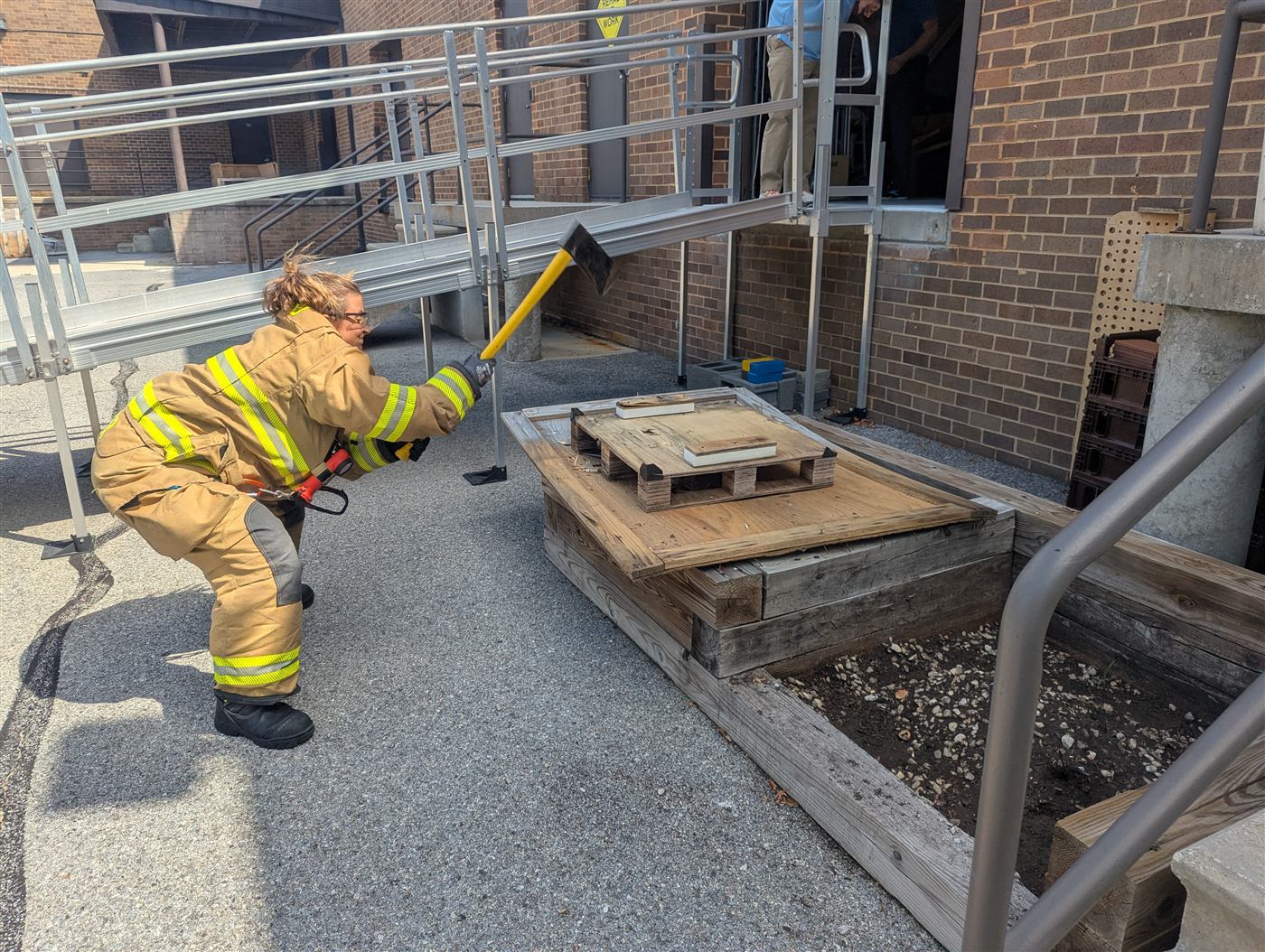 Firefighter work simulation in full turnout gear outside the Columbia clinic, REHAB AT WORK sign in frame
