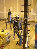 Staff member on an extension ladder mounting the yellow REHAB AT WORK diamond sign on a brick wall