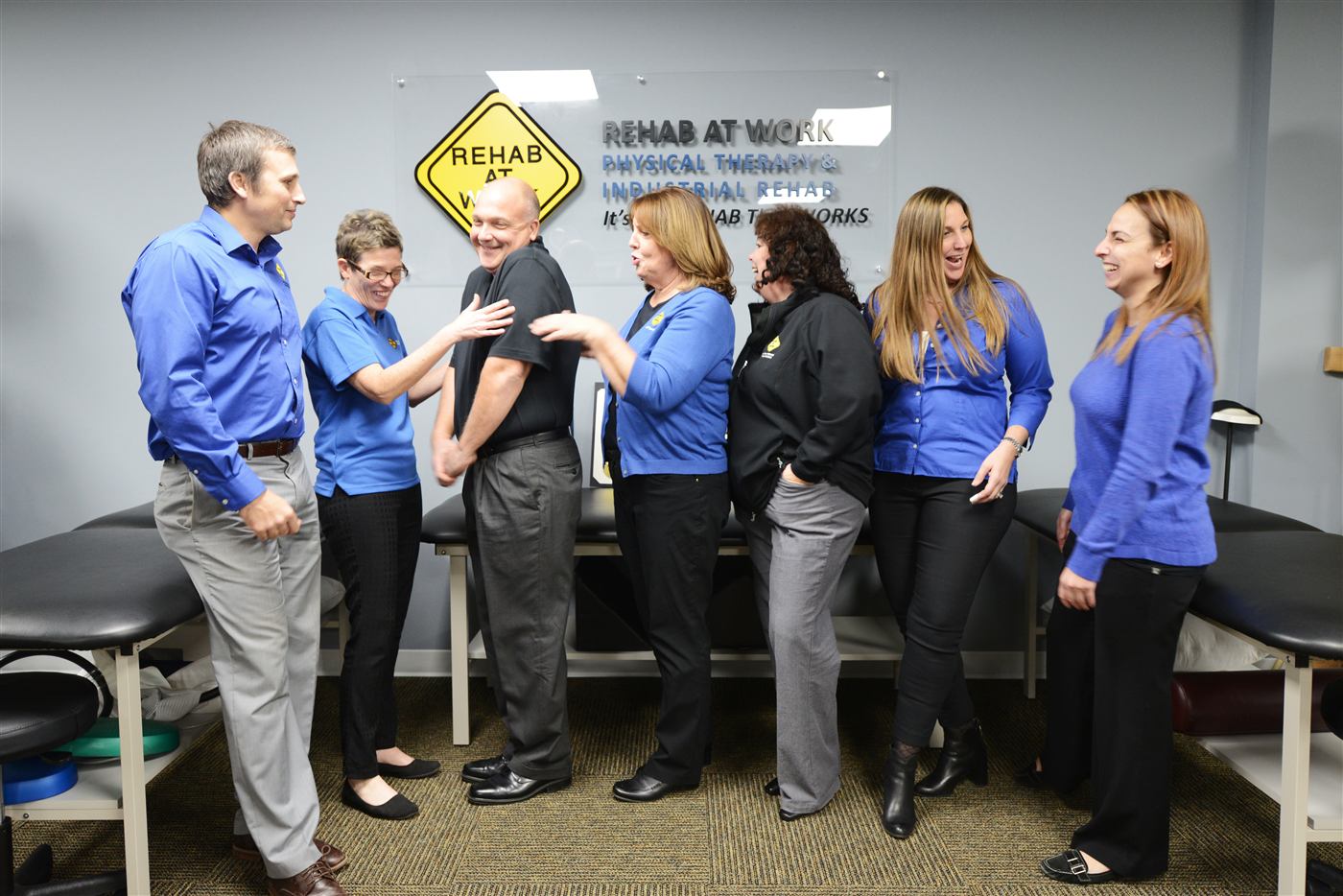 REHAB AT WORK clinicians laughing together in front of the clinic sign