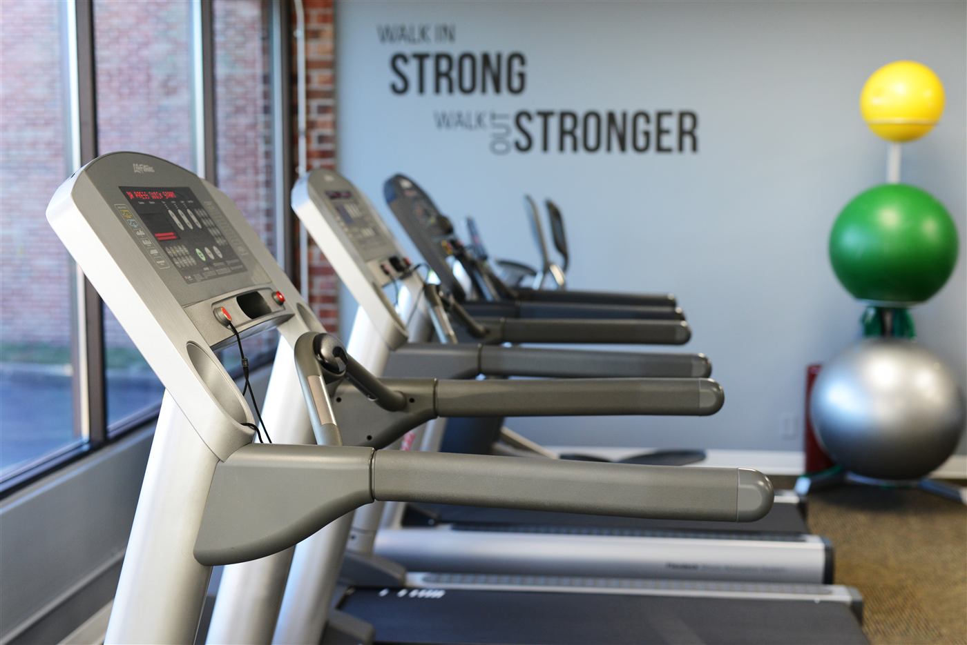 Treadmill row beneath a wall reading 'Walk in strong, walk out stronger'